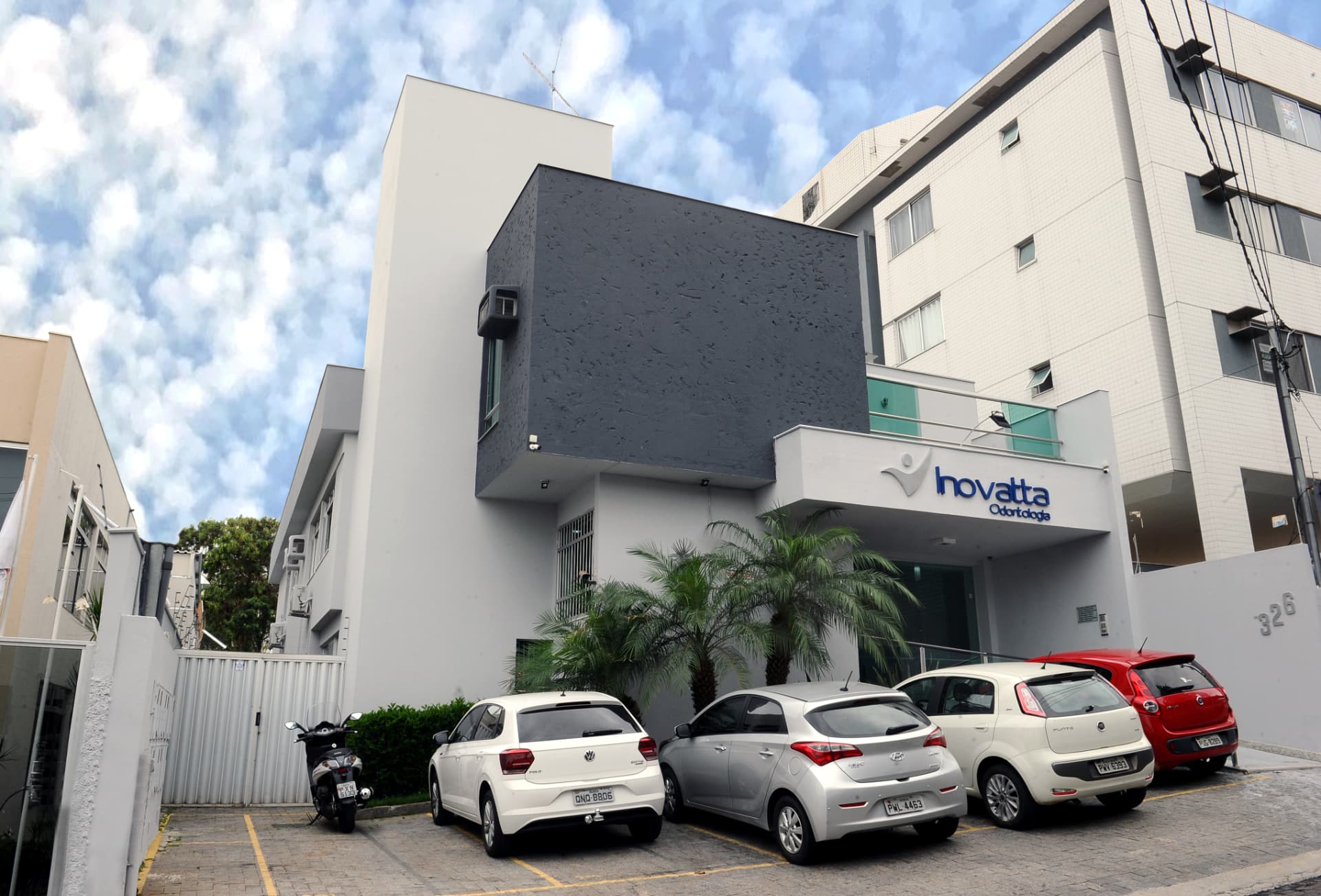 Fachada branca e cinza da clínica Inovatta Odontologia com estacionamento frontal