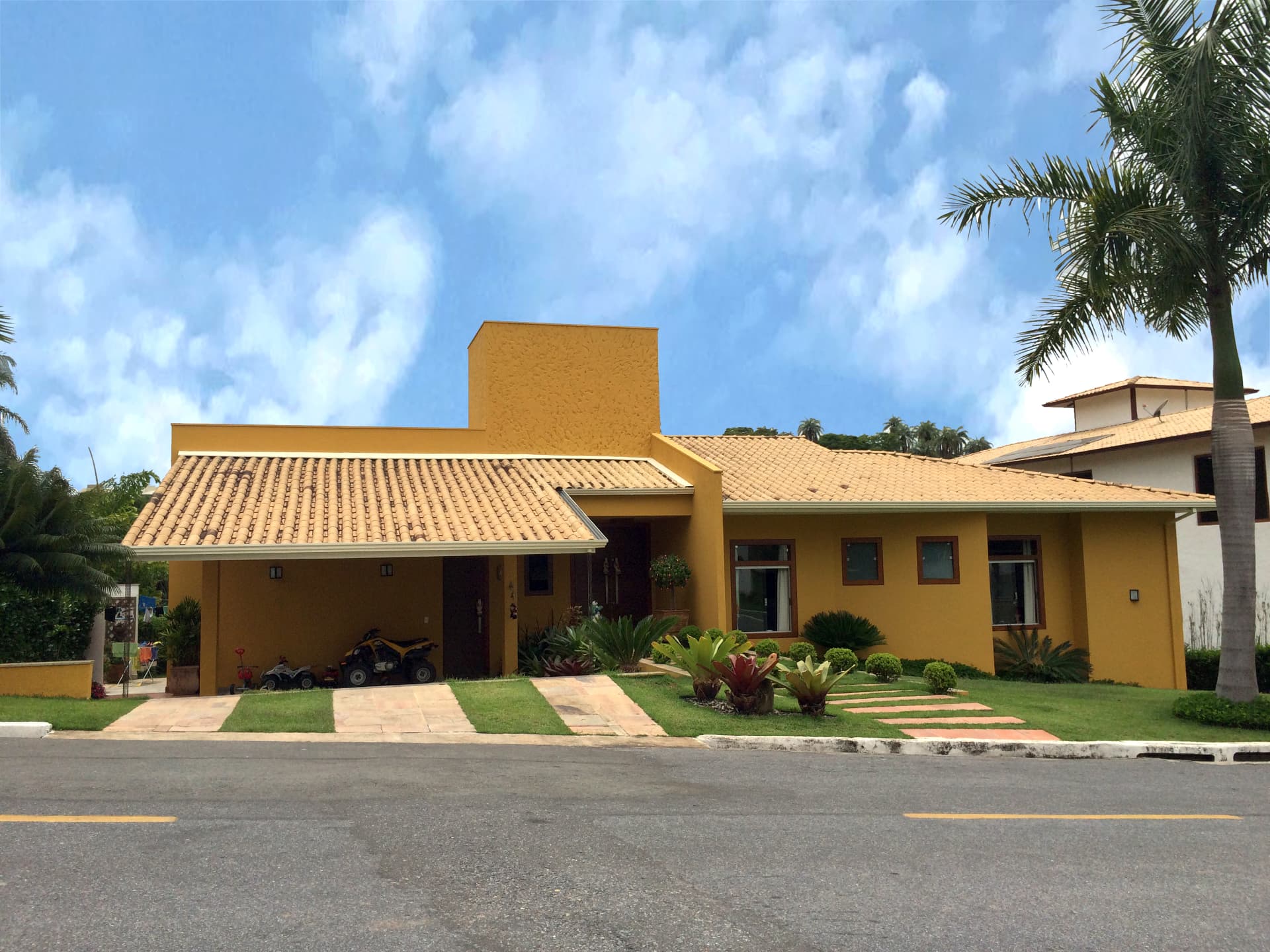 Casa térrea amarela com telhado colonial e jardim tropical
